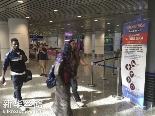 8月28日在马来西亚吉隆坡国际机场拍摄的照片显示，旅客从一块关于防范寨卡病毒传染的展示板前走过 新华社　美联　